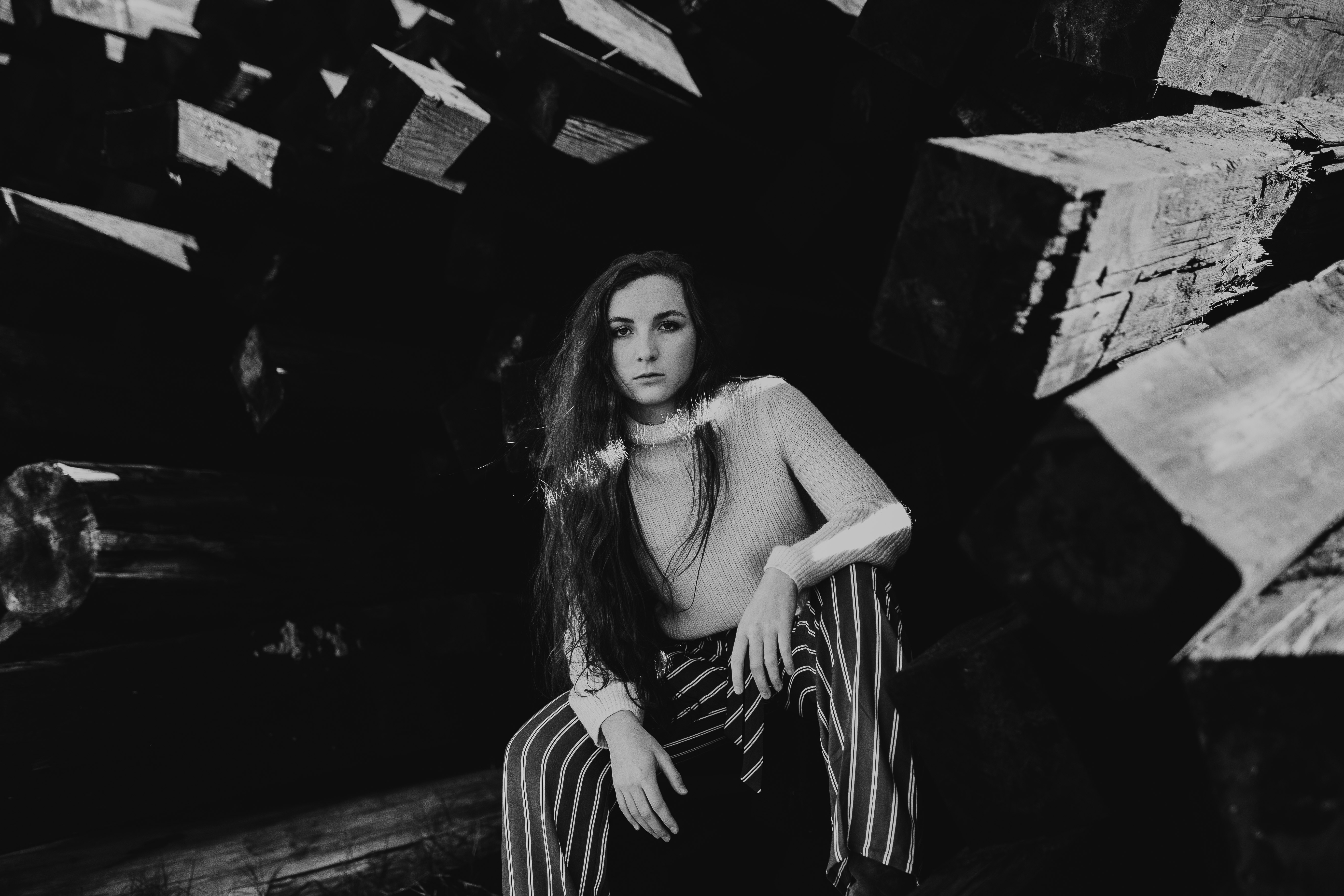 grayscale photo of woman sitting on wooden pillar